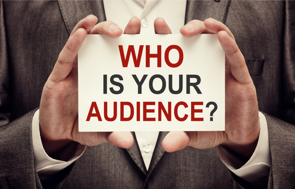 A man in a suit holding a sign that reads "Who is your audience?"